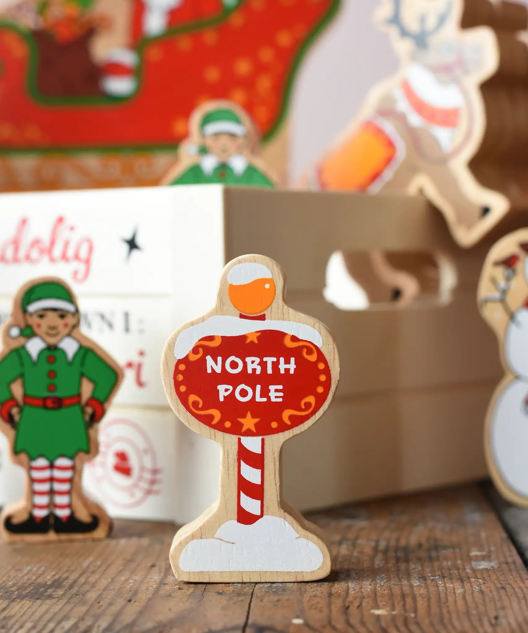 Lanka Kade red north pole sign wooden toy figure placed on a wooden surface in the Babipur playroom with other festive figures in teh background.