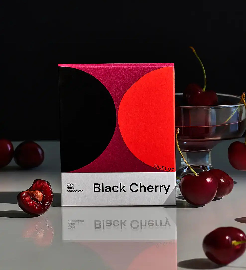 Ocelot black cherry Organic 70% Dark Chocolate in it's packaging surrounded by cherries.