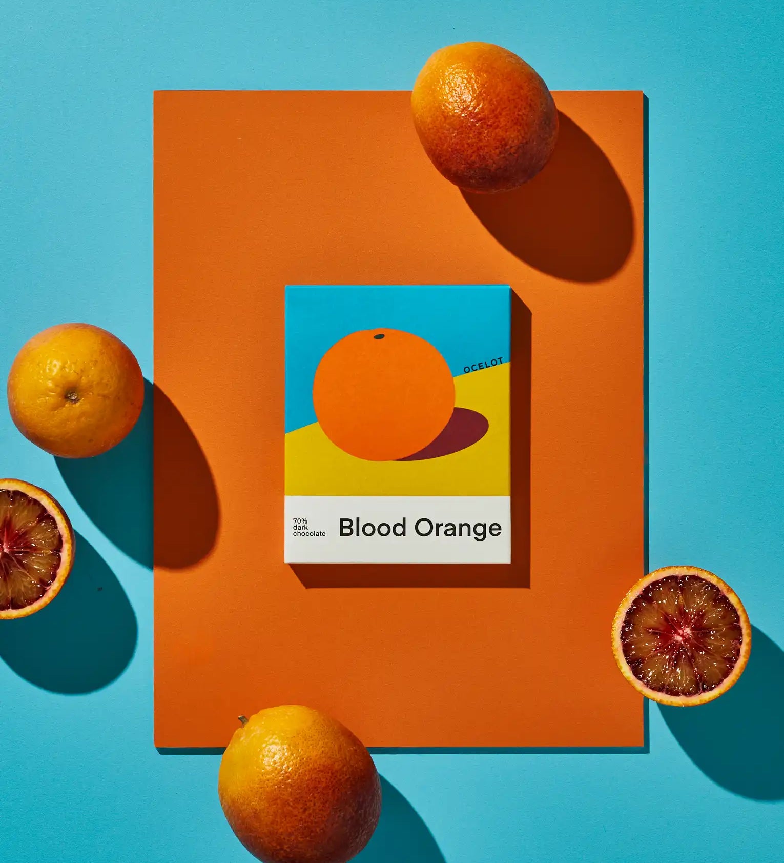 Bar of Ocelot Blood Orange Organic 70% Dark Chocolate surrounded by blood oranges some cut in half showing the flesh.