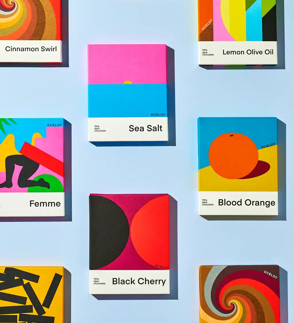Various flavours of Ocelot chocolate bars in their modern, geometric style packaging boxes. Cinnamon swirl, femme, sea salt, lemon olive oil, blood orange and black cherry varieties. 