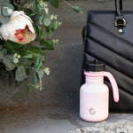 One Green Bottle 350ml plastic free water bottle on a step in front of a black hand bag and next to a white flower