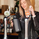 Woman holding a One Green Bottle plastic free stainless steel water bottle next to some beer pumps 