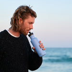Man drinking from a One Green Bottle eco-friendly metal canteen in front of the sea