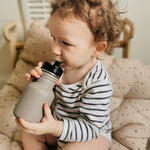 Child holding the One Green Bottle 350ml plastic free tough water bottle sat on a brown cushion