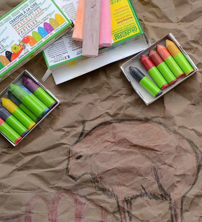 OkoNorm 12 stubby beeswax crayons placed next to cave wall themed drawings on brown paper. 

