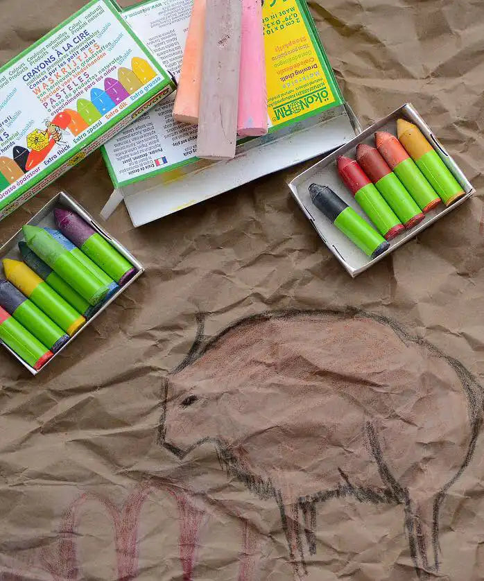 OkoNorm 12 stubby beeswax crayons placed next to cave wall themed drawings on brown paper. 
