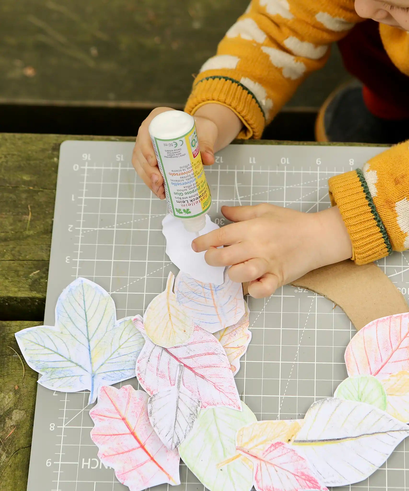 Child using the OkoNorm solvent free all purpose craft glue placing it one the back of paper leaf rubbings.