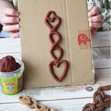 A close up of a child's hands holding up a Welsh love spoon inspired creation made using brown coloured Okonorm play dough from the earth colour set. 