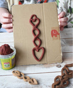 A close up of a child's hands holding up a Welsh love spoon inspired creation made using brown coloured Okonorm play dough from the earth colour set. 