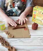 Child rolling brown Okonorm play dough into long sausage shapes. 