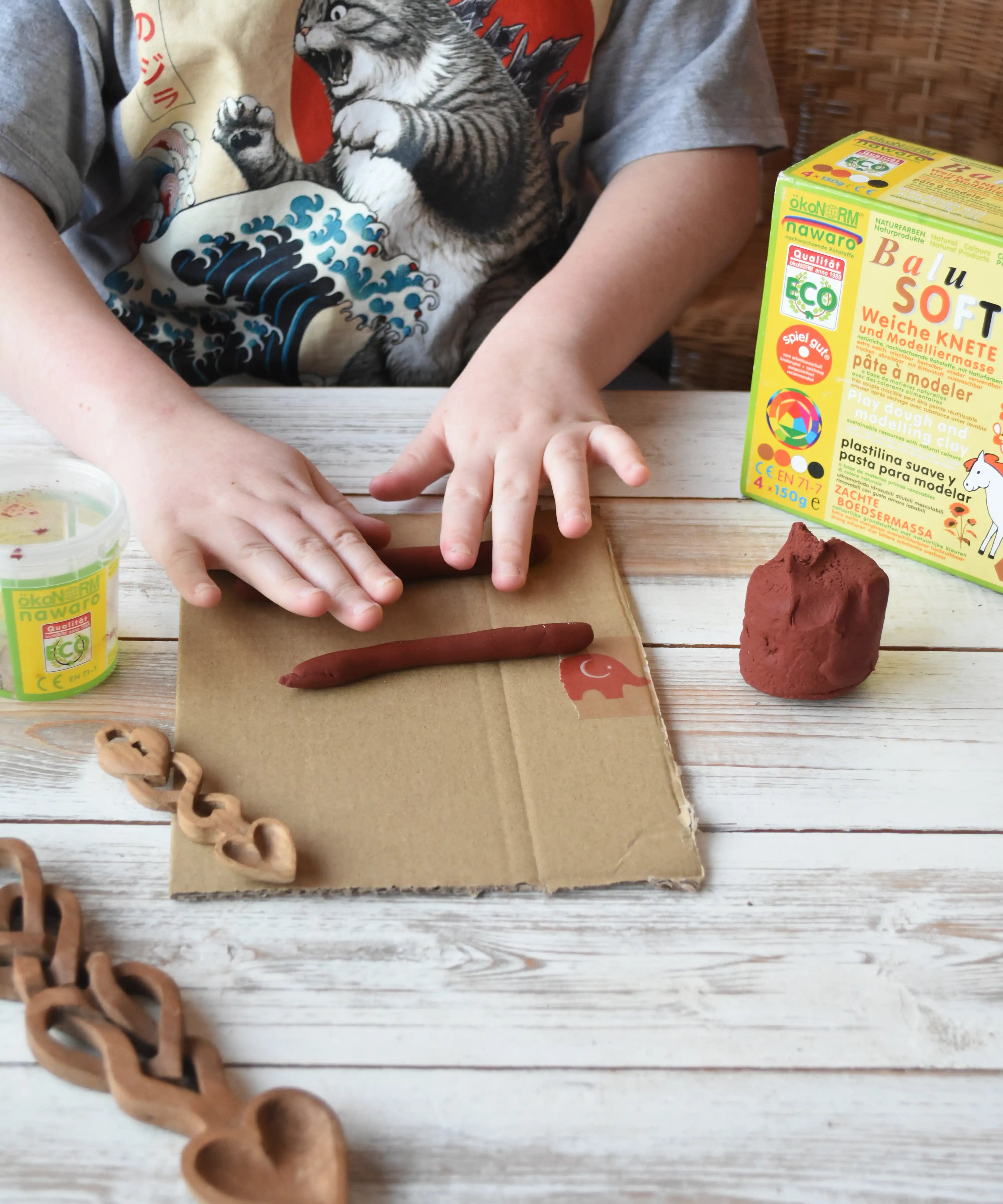 Child rolling brown Okonorm play dough into long sausage shapes. 