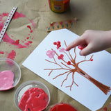 A child's hand using the Okonorm finger paints to make marks on a tree shaped crayon drawing. 