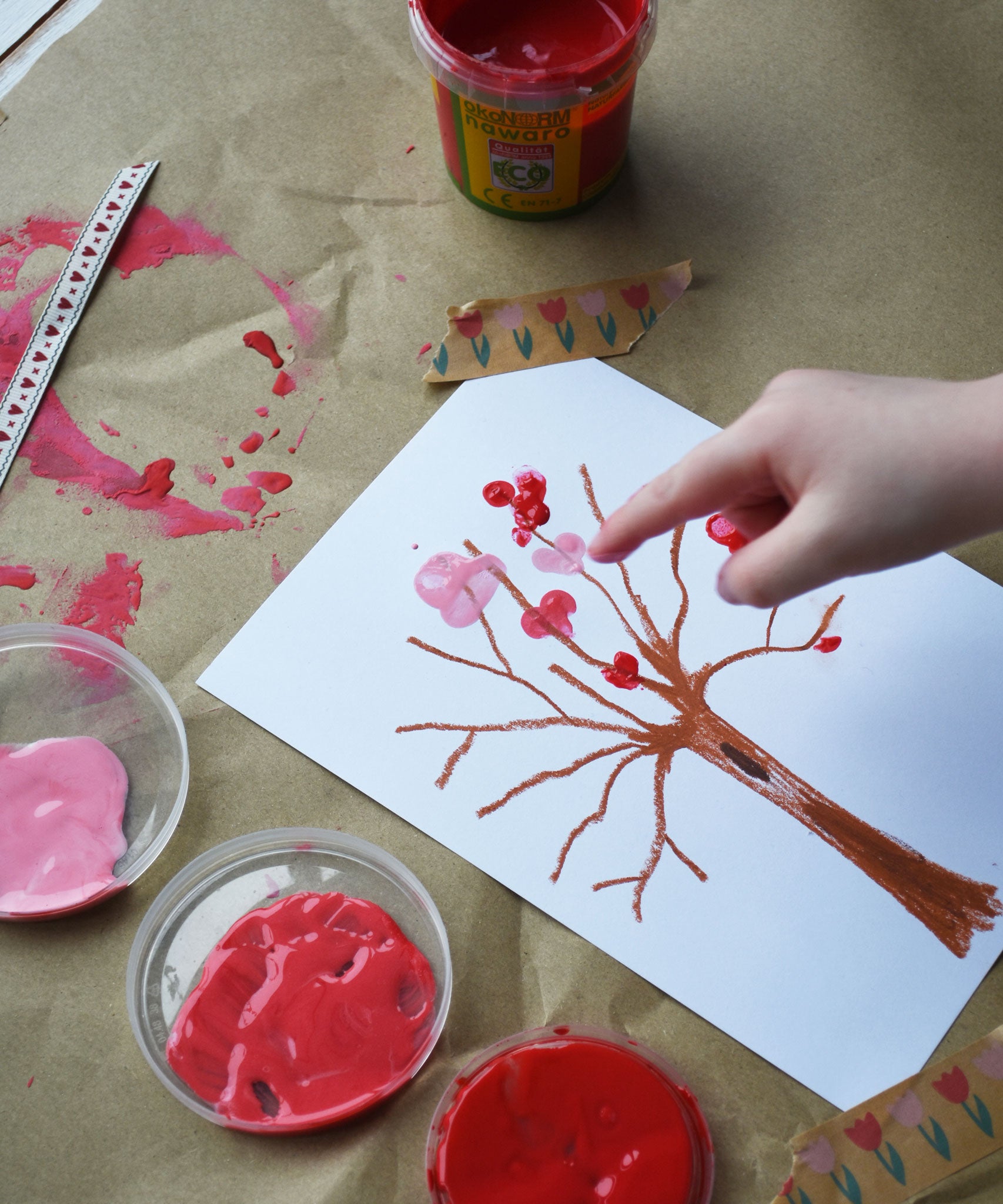 A child's hand using the Okonorm finger paints to make marks on a tree shaped crayon drawing. 