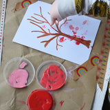 An overhead view of a young child's hands using the Okonorm finger paints to make marks on a tree shaped crayon drawing. 