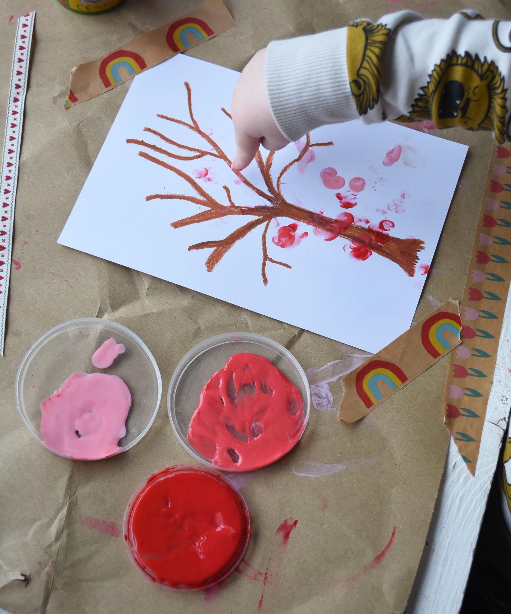 An overhead view of a young child's hands using the Okonorm finger paints to make marks on a tree shaped crayon drawing. 