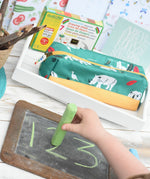 Child using a green Okonorm chalk to trace over numbers drawn on a small chalkboard.