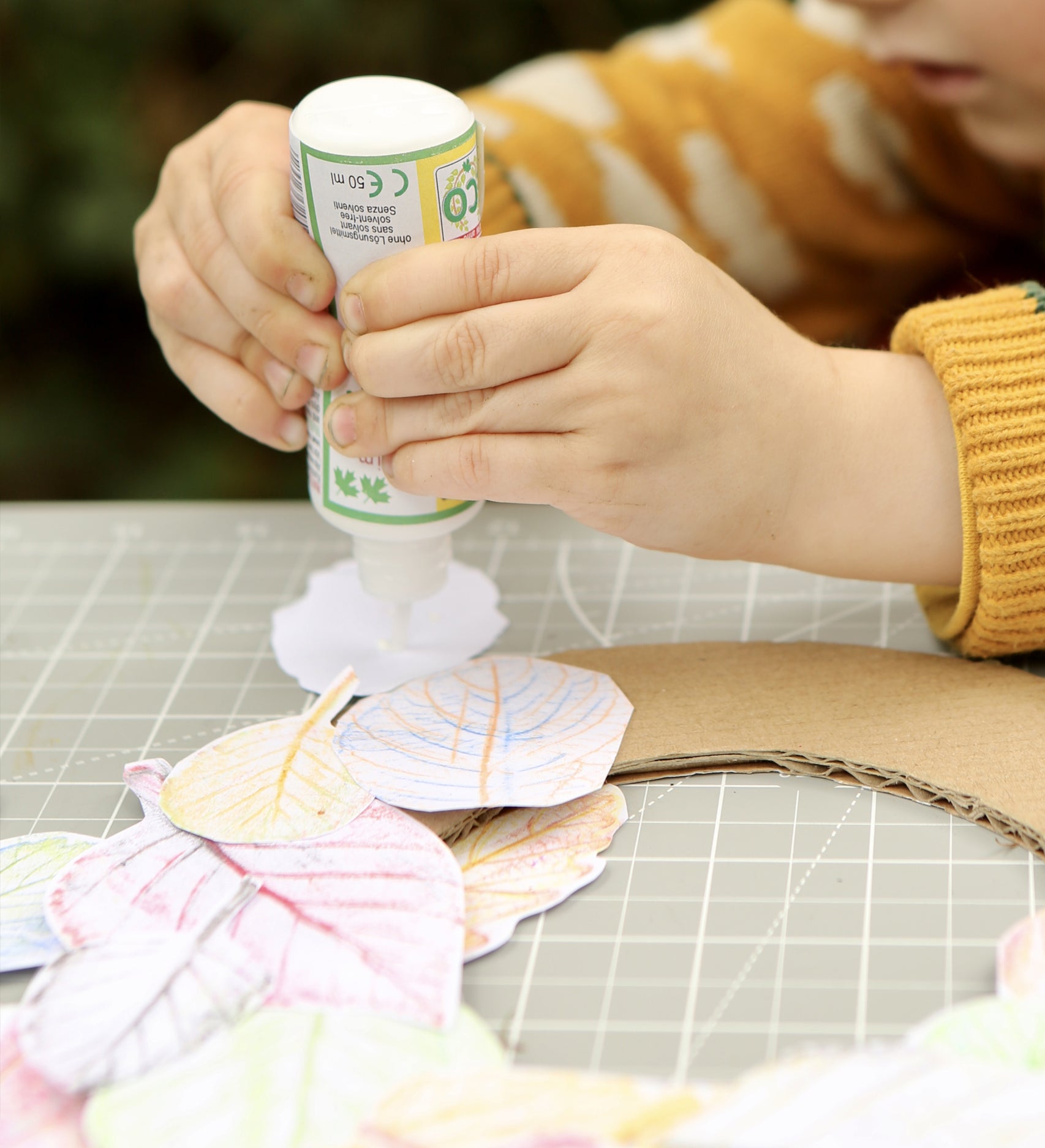 Child using the OkoNorm solvent free all purpose craft glue placing it one the back of paper leaf rubbings.