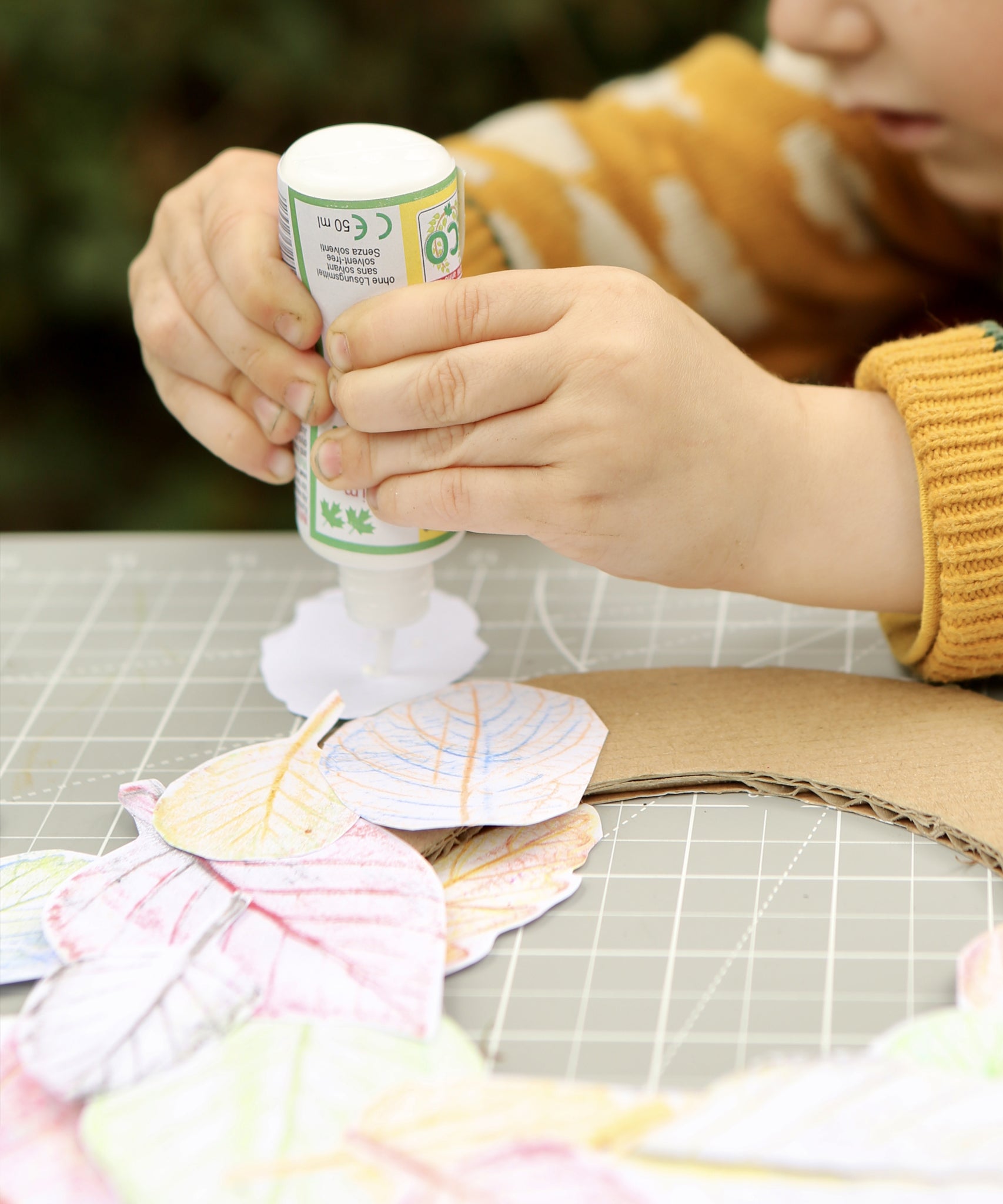 Child using the OkoNorm solvent free all purpose craft glue placing it one the back of paper leaf rubbings.