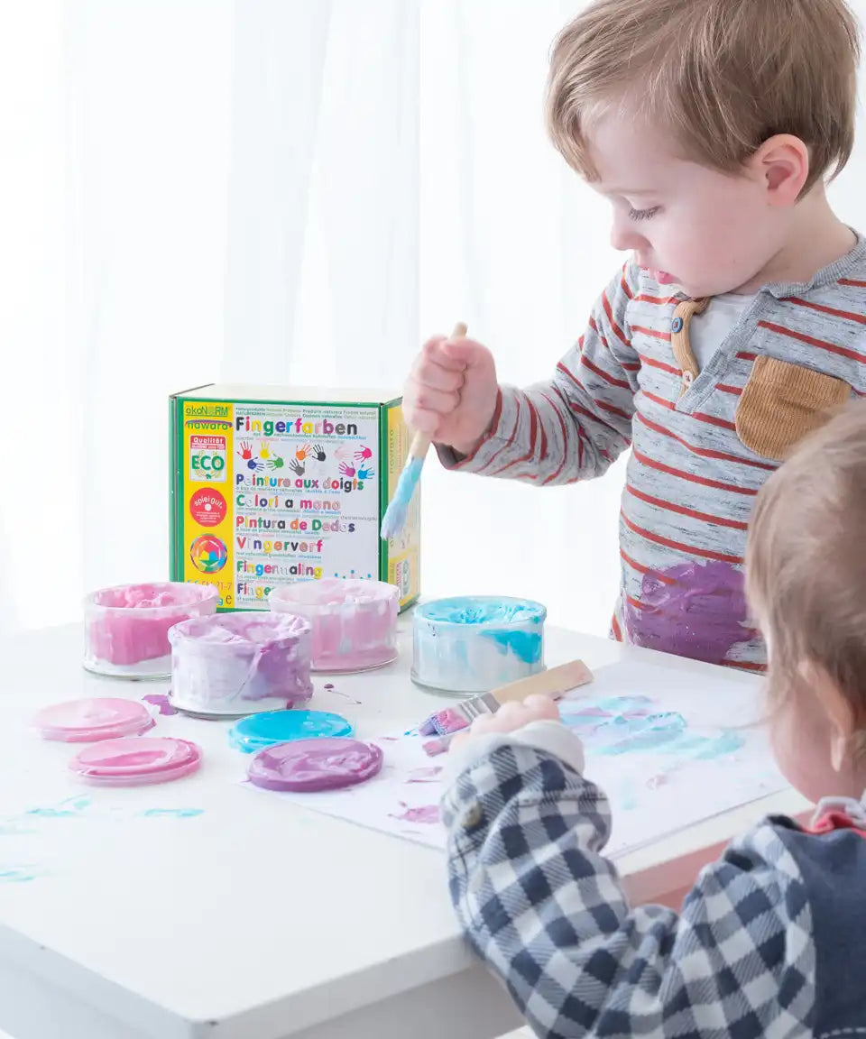 Children painting with the OkoNorm pastel colours non-toxic finger paints. One pot each of blue, purple, light pink and fuschia.