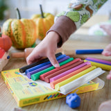 OkoNorm modelling clay in stick form in 10 colours. A child's hand can be seen picking up some of the clay sticks.