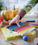 OkoNorm modelling clay in stick form in 10 colours. A child's hand can be seen picking up some of the clay sticks.