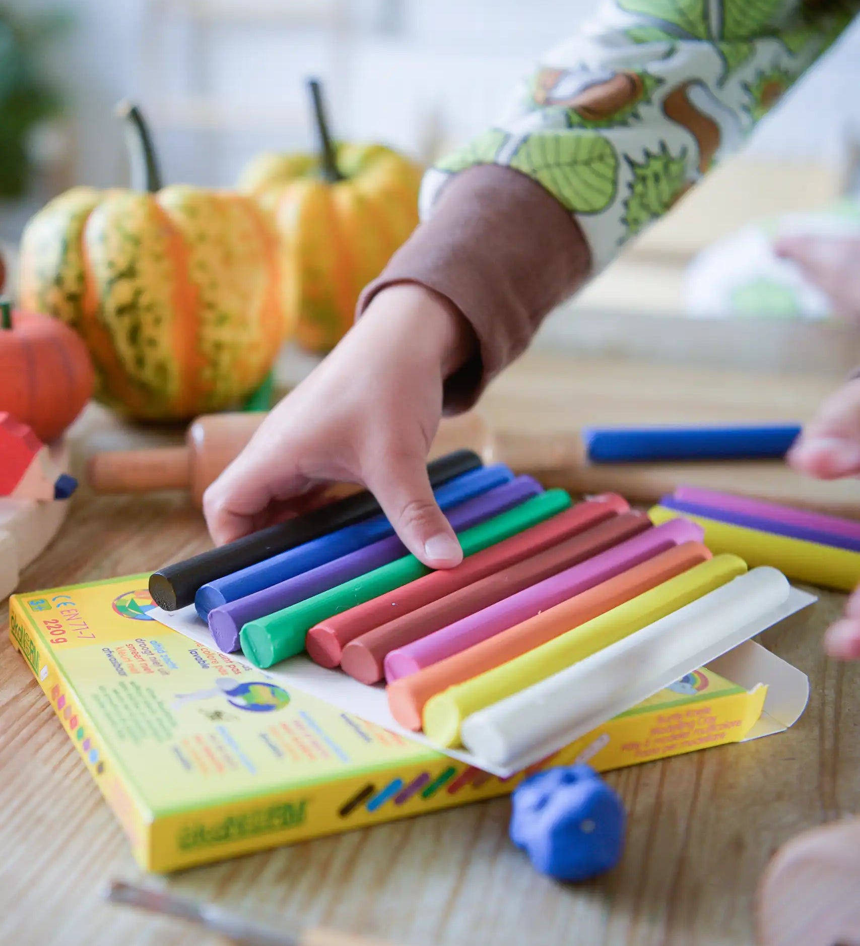 OkoNorm modelling clay in stick form in 10 colours. A child's hand can be seen picking up some of the clay sticks.