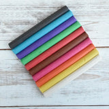 OkoNorm modelling clay in stick form in 10 colours placed on a wooden surface.