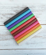OkoNorm modelling clay in stick form in 10 colours placed on a wooden surface.