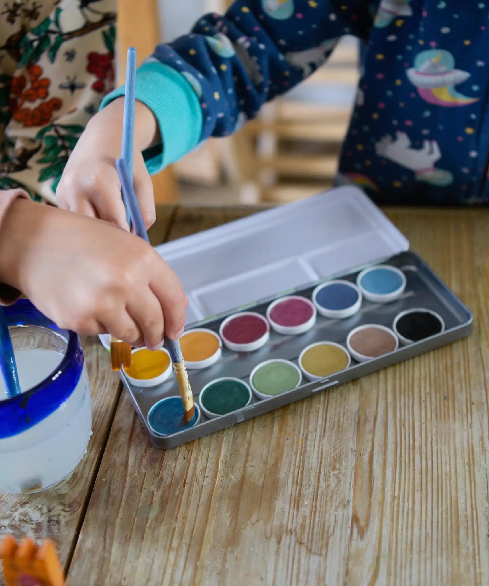 Children placing paintbrushes on the watercolour pods from the Okonorm 12 colour watercolour paints in a travel tin.