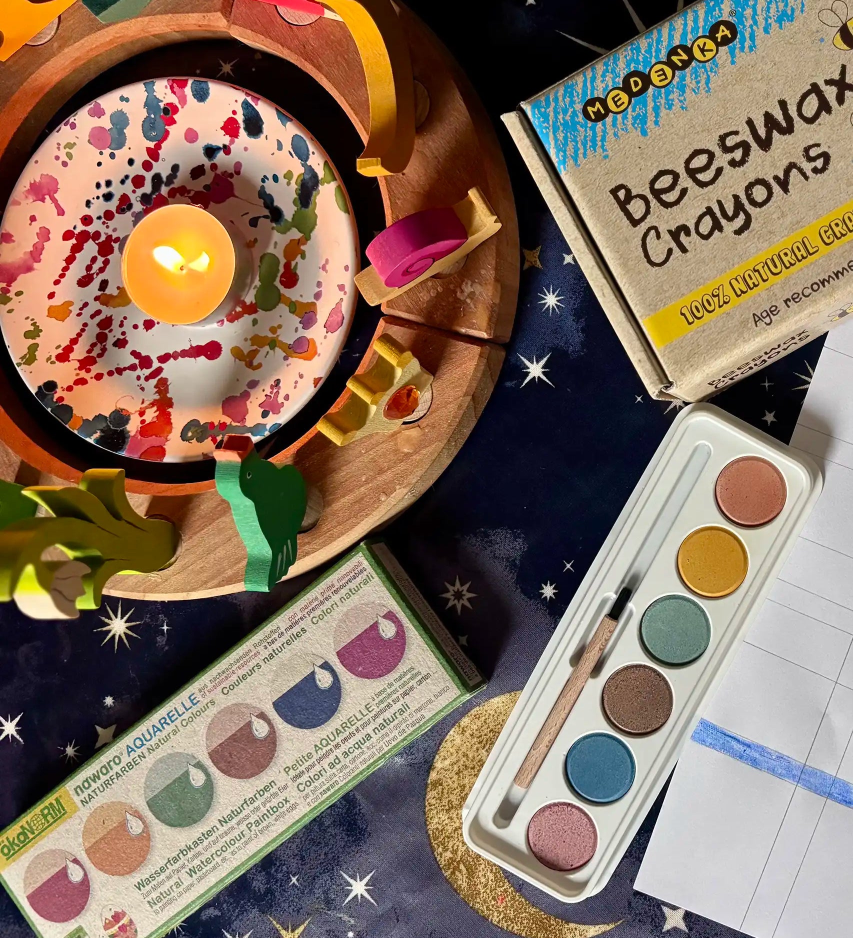 OkoNorm watercolour paints set in 6 colours placed on a table next to a decorated Grimm's celebration ring and Medenka beeswax crayons.