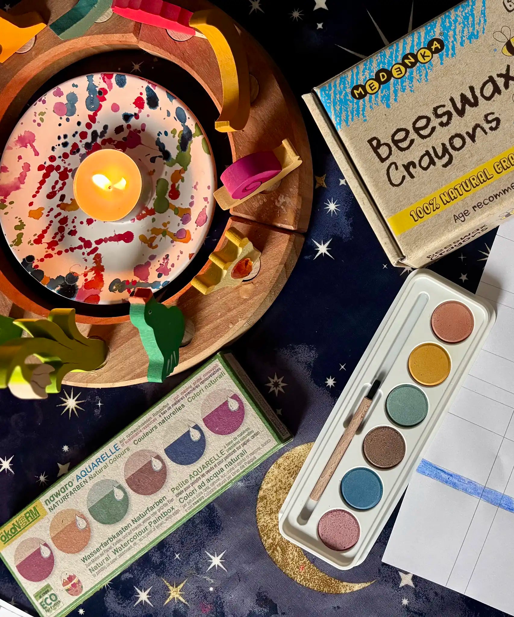 OkoNorm watercolour paints set in 6 colours placed on a table next to a decorated Grimm's celebration ring and Medenka beeswax crayons.