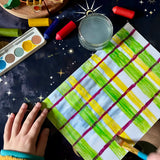 A child making a tartan style pattern using the green and yellow colours from the OkoNorm watercolour paints set to paint some of the stripes.