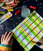 A child making a tartan style pattern using the green and yellow colours from the OkoNorm watercolour paints set to paint some of the stripes.