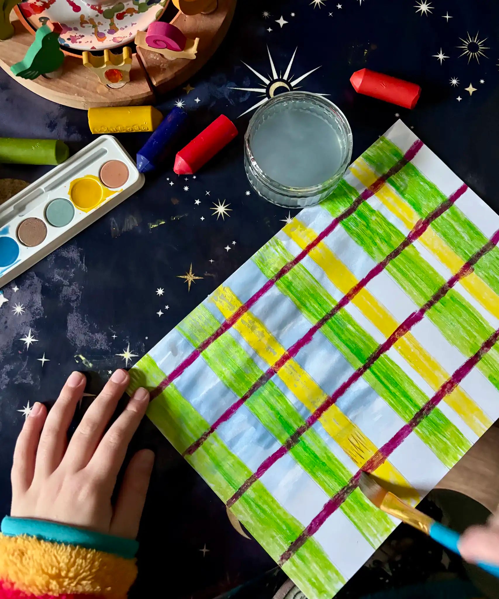 A child making a tartan style pattern using the green and yellow colours from the OkoNorm watercolour paints set to paint some of the stripes.