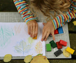 Okonorm wax blocks being used by a child. The child is sat outside in the garden and is creating leaf rubbings with the wax blocks.