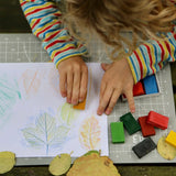 Okonorm wax blocks being used by a child. The child is sat outside in the garden and is creating leaf rubbings with the wax blocks.