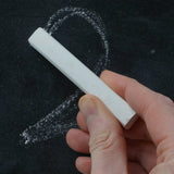 Person drawing a number 2 on a black surface with white Okonorm chalkboard chalk.