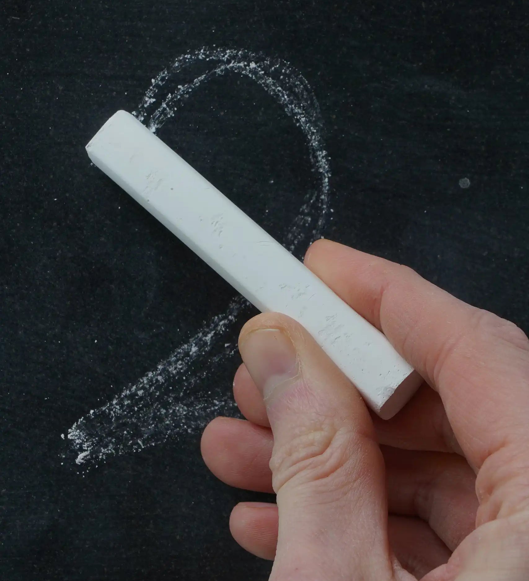 Person drawing a number 2 on a black surface with white Okonorm chalkboard chalk.