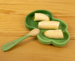 Green leaf-shaped plate with sliced bananas and a wooden spoon on a wooden surface