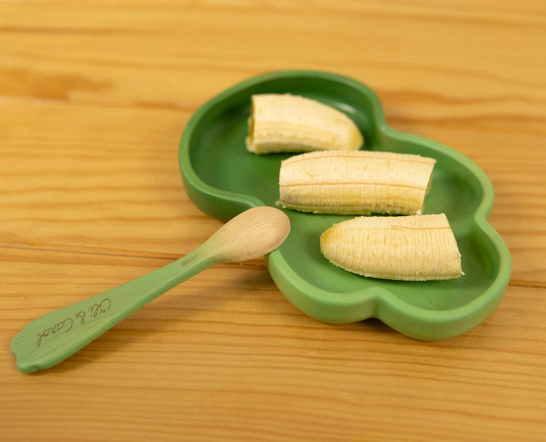 Green leaf-shaped plate with sliced bananas and a wooden spoon on a wooden surface