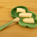 Green leaf-shaped plate with sliced bananas and a wooden spoon on a wooden surface
