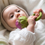 A baby clutching onto an Oli & Carol Artichoke Rattle Teether
