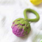 An Oli & Carol Artichoke Rattle Teether placed on white muslin