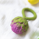 An Oli & Carol Artichoke Rattle Teether placed on white muslin