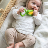 baby lying down in a changing basket clutching onto the Oli & Carol Corn Rattle Teether