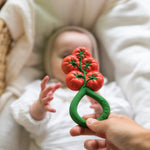 Baby lying down reaching up for an Oli & Carol Tomato Rattle Teether