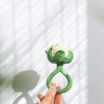 An adult's hand holding up the Oli & Carol Cauliflower Rattle Teether