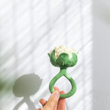 An adult's hand holding up the Oli & Carol Cauliflower Rattle Teether