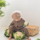 A child sitting down holding an Oli & Carol Cauliflower Rattle Teether with real cauliflowers in front of them