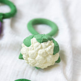 An Oli & Carol Cauliflower Rattle Teether placed an a white muslin